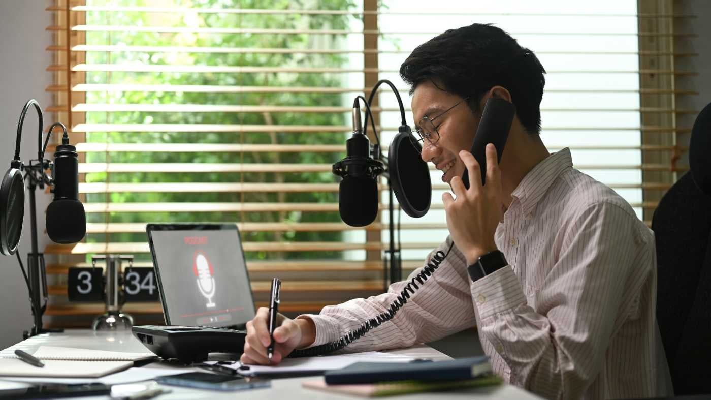 a Young Man Talking on the Phone While Recording the Call on His Laptop.
